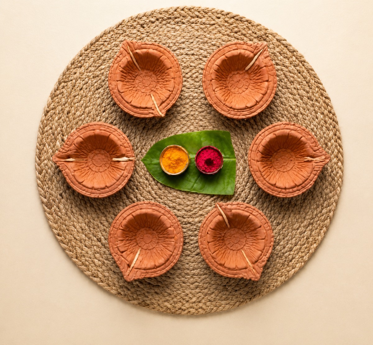 Set of six handcrafted clay diyas arranged on a woven mat