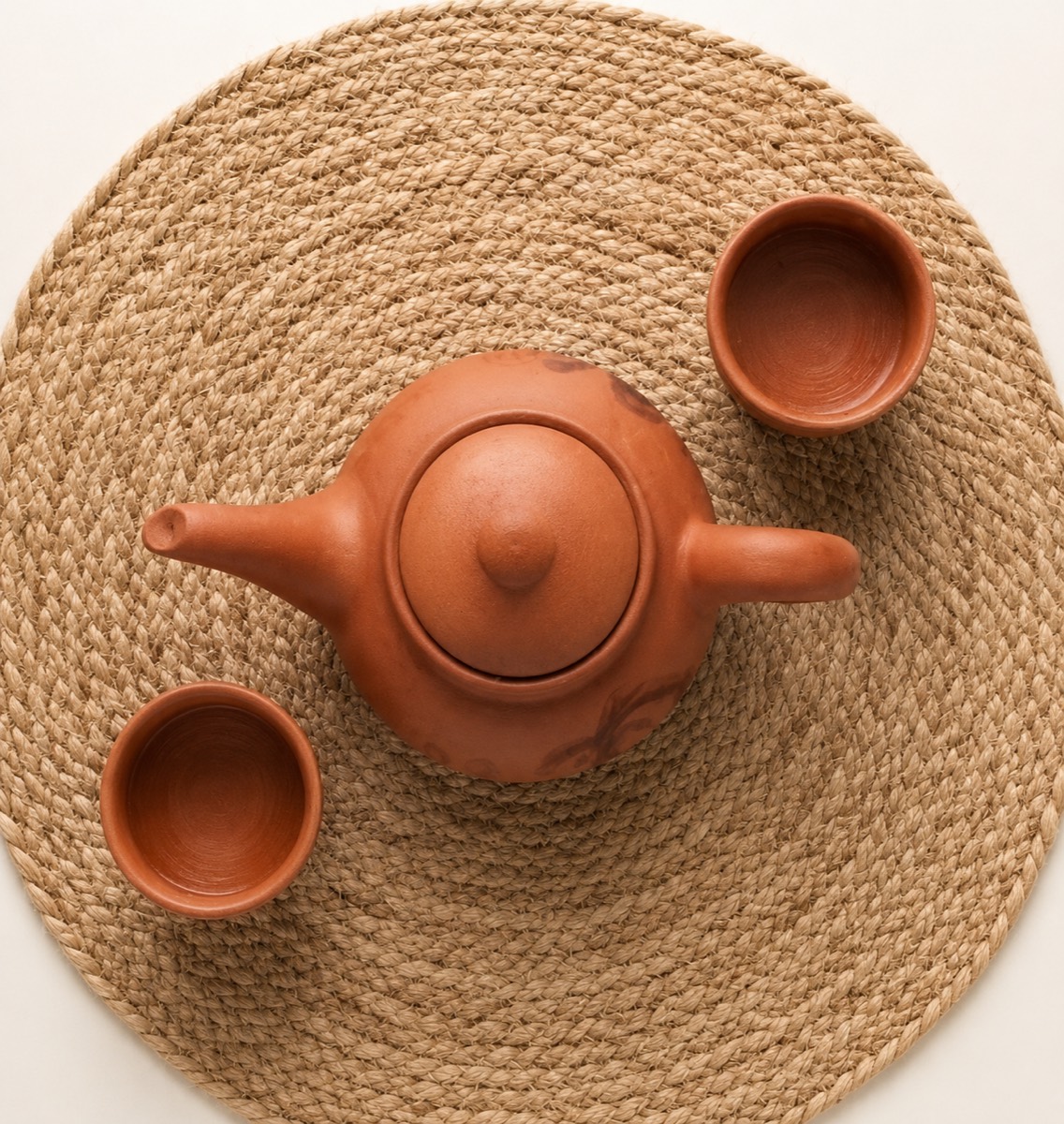 Clay teapot with two clay cups on a woven mat, top view